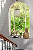 Bust of woman and candlesticks on sill of arched window with garden view in stairwell