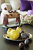 Dish of pears and plums in front of ethnic figurine