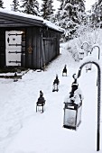 Lanterns in snow leading to black wooden hut