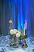 Brass candlesticks with burning candles on festively set table, in front of blue illuminated curtain in the background