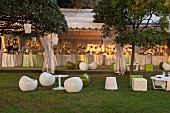 Designer outdoor seating in green and white around round tables on the lawn, in the background festively set tables in a row under a white tent roof