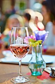 Glass of rosé wine in front of vase of flowers