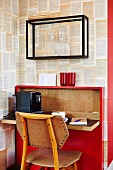 Chair at small red bureau with fold-down desk against wall covered in designer wallpaper