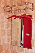Retro metal coat rack in front of mirror on wall with patterned wallpaper