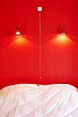 Bed below spotlights on bright red wall