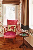 Floral scatter cushion on pink velvet armchair next to delicate, antique, wooden side table below window in corner