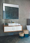 Floating washstand and seagrass baskets against concrete wall and below mirror reflecting slate tiles