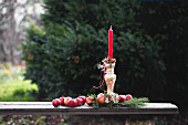 Red apples and pine cones around red candle in silver candlestick