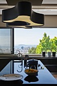Black glossy kitchen counter in front of large windows with view of city and sea