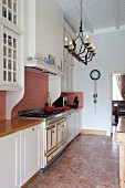 Kitchen counter with white base units in elegant country-house style and ornate chandelier suspended from white wood-beamed ceiling