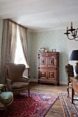 Antiker Ohrensessel mit hellbraunem Stoffbezug und kunsthandwerklicher Schrank in traditionellem, elegantem Wohnzimmer