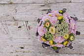 Blumengesteck aus Chrysanthemen und Schafgarbe auf rustikaler Holzunterlage