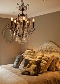 Crystal chandelier above bed with vintage-style scatter cushions and curved headboard in romantic bedroom