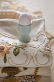 White hen's egg in turquoise eggcup on embroidered tablecloth