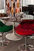 Retro shell chairs made from coloured transparent plastic around Tulip Table with place settings