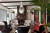 White leather armchairs and black plastic shell chairs below classic pendant lamp in open-plan retro interior