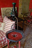Rustic plant stand painted red next to daybed with ornate, vintage-style metal frame