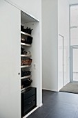White fitted cupboard with view of shoe shelves through open sliding door in modern hallway