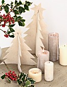Hand-made felt Christmas trees, lit candles and sprigs of holly on concrete table