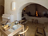 Set table next to open fire in arched niche with masonry shelves and platforms in Apulian trullo