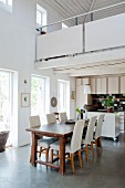 Wooden table and pale upholstered chairs in dining area of open-plan kitchen below white gallery