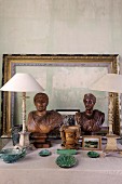 Arrangement of ceramic objects, antique table lamps with white lampshades, wooden busts and picture frames