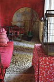 Mediterranean interior with red walls, pebble mosaic, daybed, birdcage and floral tablecloth on table