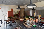 Geschirr auf Kücheninsel mit Gaskochfeld unter Pendelleuchten im Vintagestil, im Hintergrund Essplatz in modernem ländlichem Ambiente