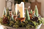 Christmas arrangement of small fir trees, animal figurines and white pillar candle