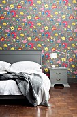 Grey double bed and bedside table against floral wallpaper