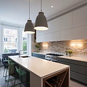 Fitted kitchen with white wall units, pendant lamps above island counter and green bar stools