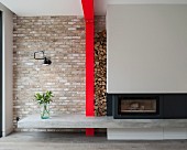 Modern fireplace with concrete hearth, firewood stacked between grey chimney breast and red steel column against brick wall