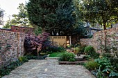 Well-tended garden of terrace house with paved area, herbaceous borders and brick walls