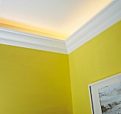 Indirect lighting secreted above white DIY stucco moulding on yellow walls