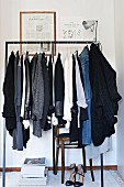 Woman's clothing hung on minimalist metal clothes rail above blac high heels in corner