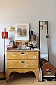 Clutter of objects on top of chest of drawers between standard lamp and narrow full-length mirror