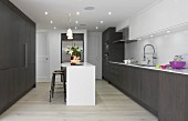 Fitted kitchen with dark brown cupboards, white island counter, recessed spotlights and white wall cabinets in elegant interior