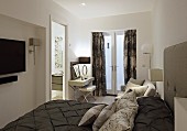 Elegant double bed with dark brown bedspread and arranged scatter cushions and dressing table in front of French windows