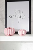 Pink paper ornaments and black-framed motto on white floating shelf