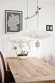 String of wooden beads on white wooden frame behind wooden table, bowl of flowers and pendant lamps