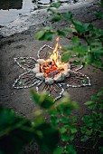 Romantic campfire on river bank surrounded by flower pattern of stones and sticks