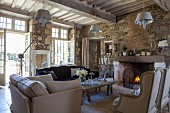 Elegant armchairs in front of open fire and open terrace doors in living room of rustic country house