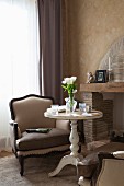 Vase of white tulips on round vintage side table and elegant armchair next to fireplace