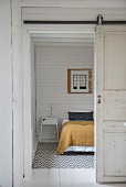Offene Schiebetür und Blick auf Bett in schlichtem Schlafzimmer mit weisser Holzwand