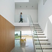 Staircase with glass balustrade in minimalist interior with dining table in front of sliding terrace doors in background