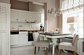 Dining table for two with upholstered chairs below window in white fitted kitchen