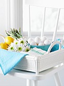 Eier, Spargel, Zitronen und Blumen im Korb auf weißem Stuhl