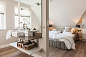 Schmaler Raumteiler mit integriertem Waschtisch, dahinter Doppelbett in offenem Schlafzimmer in beige Tönen