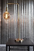 Elegant brass table lamp with glass lampshade in front of shiny metal wall