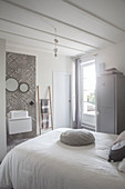 White bedspread on bed and washstand against ornate grey wall-tiles in restored bedroom